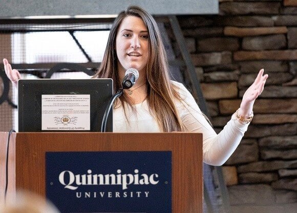 Filomena Stabile stands behind a podium with a laptop on it talking to a room of people.