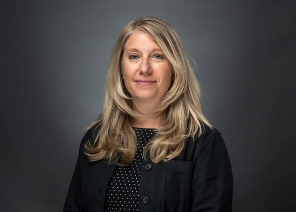 Professor Jennifer Dauphinais smiles in a black jacket and black and white polka dotted shirt.